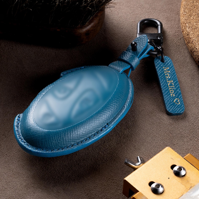 A blue leather car keychain with a keyring attached, resting on a surface with other items.