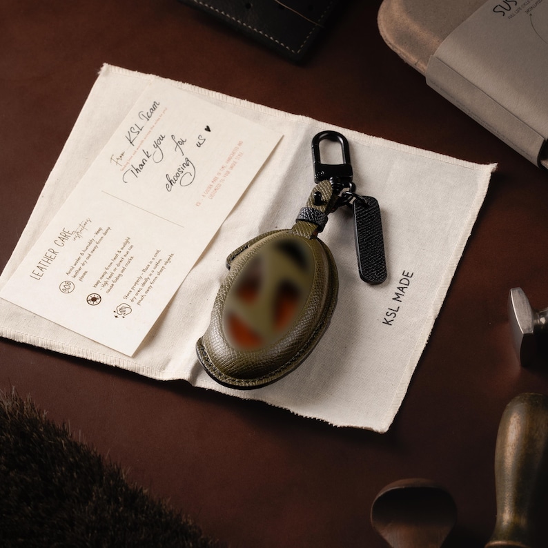 a leather case with a keychain attached to it, placed on a table. There is also a piece of paper with text and a keychain on it, which is lying on the table.