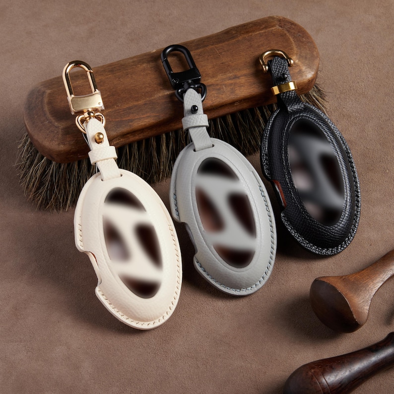 three leather keychains hanging on a wooden hanger, each with a different color and design.