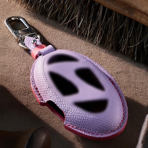 A purple leather keychain with a pink clasp and a silver hook is shown in the image.
