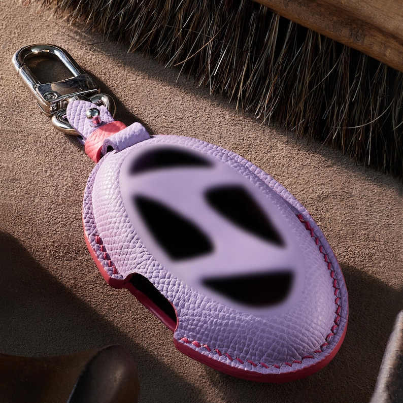 A purple leather keychain with a pink clasp and a silver hook is shown in the image.