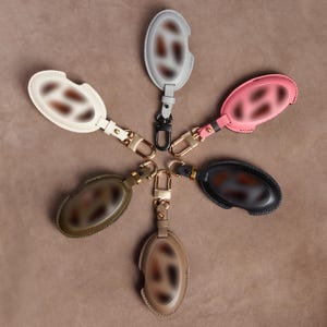 A collection of six leather keychains in various colors arranged in a circular pattern on a beige background.