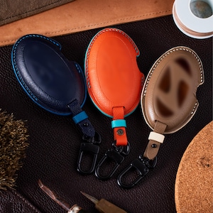three leather car key covers in different colors - blue, orange, and brown.