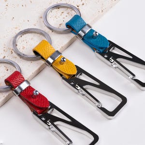 May include: Three leather keychains in red, yellow, and blue. Each keychain features a metal clasp and a leather strap with a metal rivet. The key rings are silver.