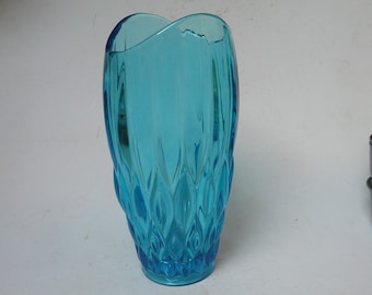 May include: A blue glass vase with a textured, wavy design. The vase is shaped like a heart at the top and has a rounded bottom.