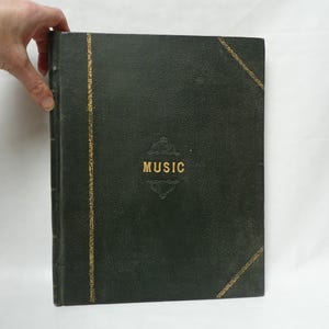 Puede incluir: Un libro de música encuadernado en cuero verde oscuro con detalles dorados y la palabra "MUSIC" en relieve en la portada.
