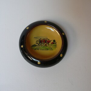 May include: A black and yellow ceramic dish with white polka dots. The dish has a yellow interior with a cartoon image of people walking with the text "Off to Widecombe Fair".