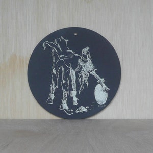 May include: A black circular slate board with a white drawing of two figures. One figure is a person with a top hat and the other figure is a person with a long tail. The figures are drawn in a whimsical style and are surrounded by white lines.