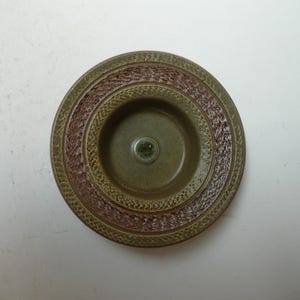 May include: A green ceramic bowl with a brown rim and a textured design. The bowl has a small, round indentation in the centre.