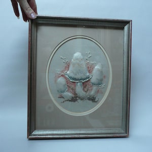 May include: A framed embroidery of mushrooms in shades of white, green, and pink. The mushrooms are surrounded by a light brown background and are set within a circular frame.