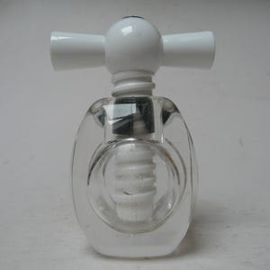 May include: A clear glass corkscrew with a white handle and a white screw. The corkscrew has a bulbous body and a cross-shaped handle. The screw is visible through the glass.