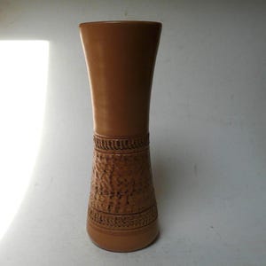 Puede incluir: Un jarrón de cerámica marrón con un diseño texturizado y una base ancha. El jarrón mide aproximadamente 25 cm de alto.