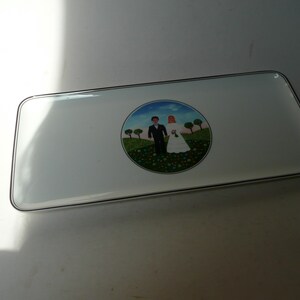 May include: White rectangular ceramic serving tray with a black rim. The tray features a painted scene of a bride and groom in a green field with trees and flowers.