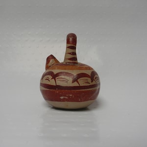 May include: A small, round, brown and white ceramic pot with a narrow neck and a decorative design. The pot has a brown and white geometric pattern around the middle.