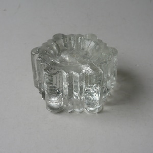 Może przedstawiać: Szklany świecznik z przezroczystego szkła z wzorem gwiazdy. Świecznik ma teksturę, żebrowaną powierzchnię i okrągły otwór w środku.