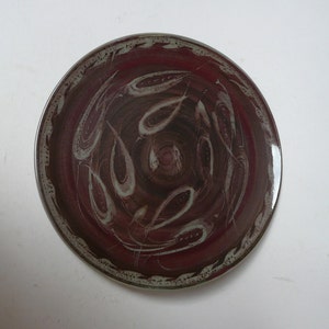 May include: A round ceramic plate with a brown and white swirl design. The plate has a raised rim and a white border.