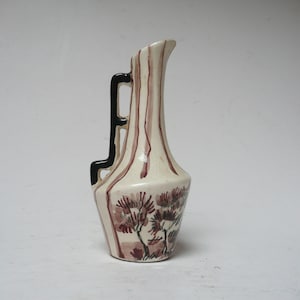 May include: A small white ceramic pitcher with a black handle and brown painted stripes and floral designs.