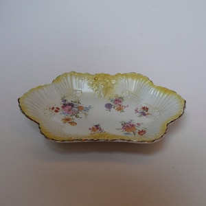 Puede incluir: Un plato de servir de porcelana blanca con un borde festoneado y un patrón floral en tonos de rosa, amarillo y azul. El plato tiene un borde dorado.