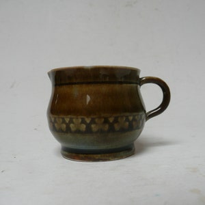 Puede incluir: Una taza de cerámica marrón con un esmalte verde y un patrón de pequeños corazones alrededor del centro.