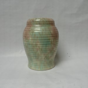 May include: A green and brown ceramic vase with a ribbed texture. The vase has a rounded shape and a wide mouth.