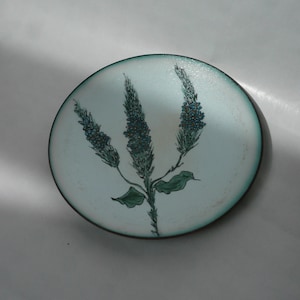 Puede incluir: Un plato de cerámica blanco con un borde verde y un diseño pintado a mano de una rama de flores azules.