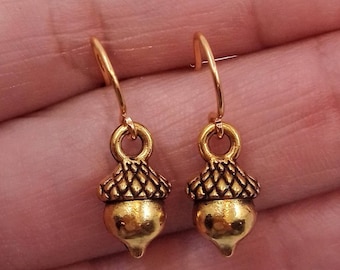 May include: A pair of gold acorn dangle earrings. The acorns are detailed with a textured surface and have a shiny finish.