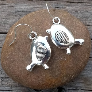 May include: A pair of silver bird earrings with a textured design. The earrings are hanging from a silver hook.