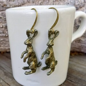 May include: A pair of gold-toned earrings featuring a detailed rabbit design. The rabbits are standing on their hind legs with their front paws raised.