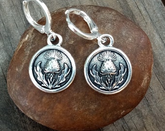 May include: Silver hoop earrings with a silver charm featuring a detailed thistle design.