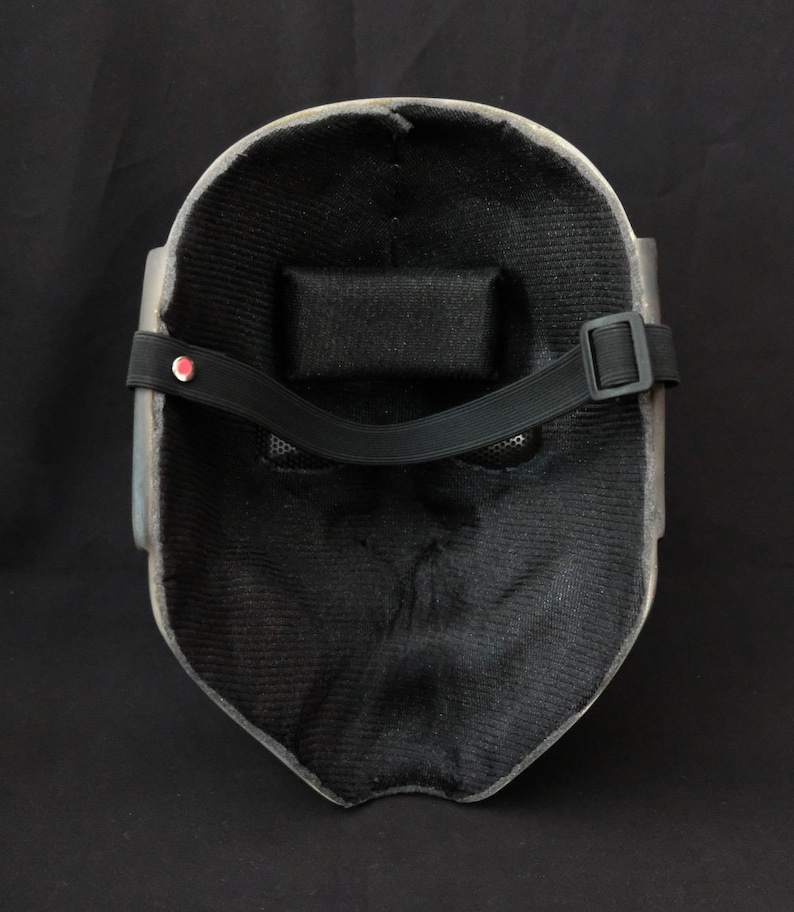 May include: A black and gray mask with a black strap and a mesh covering the eyes. The mask is made of a hard material and has a textured surface.