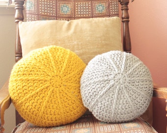 Puede incluir: Un sillón marrón con tapicería de tela estampada. Dos cojines redondos de punto, uno amarillo y otro gris, están en el sillón. Una figurita de oso de madera está en un estante en el fondo.