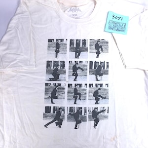 May include: Off-white XXL t-shirt featuring a black and white sequence of a man in a suit walking up stairs. The shirt has a crew neck and short sleeves. The brand name is visible at the top of the shirt.