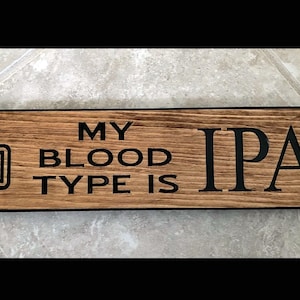 May include: Wooden sign with the text "My blood type is IPA+" and a black and white illustration of a beer mug.