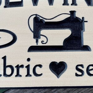 May include: Wooden sign with a black silhouette of a sewing machine and the text "Sewing is my fabric to sew".