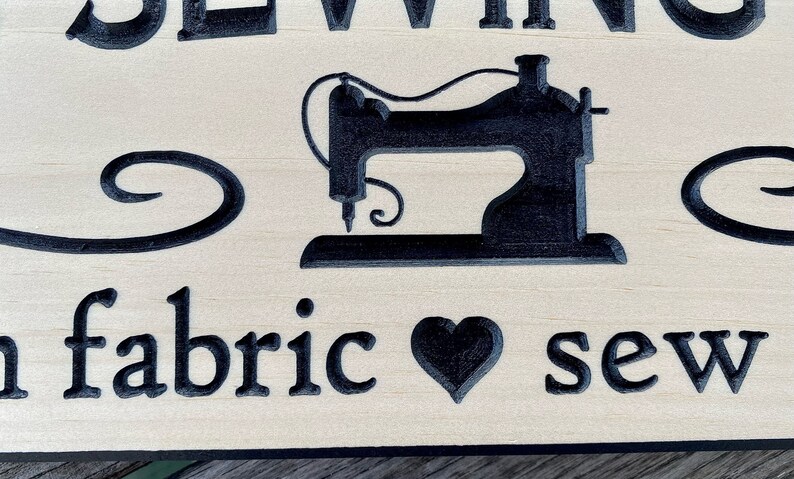 May include: Wooden sign with a black silhouette of a sewing machine and the text "Sewing is my fabric to sew".