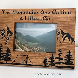 May include: Wooden picture frame with a black silhouette of mountains, trees, and a tent. The frame has the text "The Mountains Are Calling & I Must Go" engraved on the top.