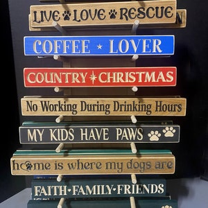 May include: A set of wooden signs with various sayings, including "home is where my honey bee", "LIVE LOVE RESCUE", "COFFEE LOVER", "COUNTRY CHRISTMAS", "No Working During Drinking Hours", "MY KIDS HAVE PAWS", "home is where my dogs are", "FAITH FAMILY FRIENDS", and "HOME IS WHERE MY CAT IS".