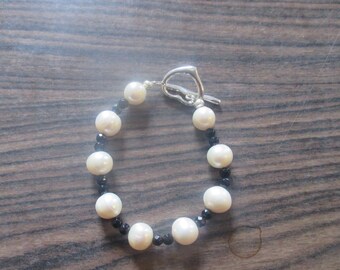 May include: A white pearl and black bead bracelet with a silver heart-shaped clasp.