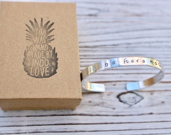 May include: Silver cuff bracelet with the words "be here now" engraved on it. The bracelet is packaged in a small brown box with a pineapple design and the words "This was hand made by Indo Love".