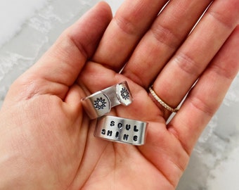 Puede incluir: Dos anillos de plata con un diseño de sol y las palabras "Soul Shine" grabadas en ellos.