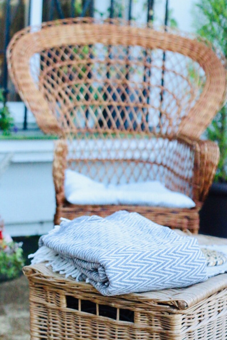 May include: A gray and white striped throw blanket folded on top of a wicker ottoman. The ottoman is in front of a wicker peacock chair.