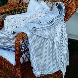 May include: A wicker chair with a gray and white patterned throw blanket draped over it. The blanket has white fringe and a chevron pattern.