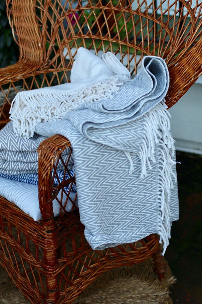 May include: A wicker chair with a gray and white patterned throw blanket draped over it. The blanket has white fringe and a chevron pattern.