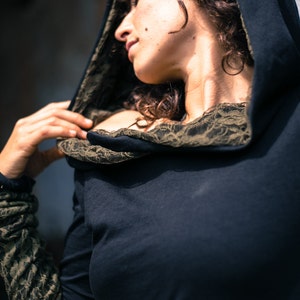May include: A black hooded top with a lace trim around the neckline. The hood is pulled up and the top is worn over the shoulders.