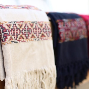 May include: Three woven shawls with fringe, one white with red and black geometric patterns, one dark blue with red and black geometric patterns, and one red with black geometric patterns.