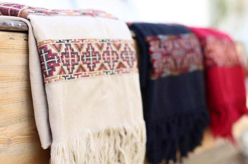 May include: Three woven shawls with fringe, one white with red and black geometric patterns, one dark blue with red and black geometric patterns, and one red with black geometric patterns.