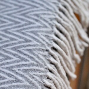 May include: A white blanket with a chevron pattern and fringe trim. The blanket is soft and fluffy, and it would be perfect for cuddling up on the couch.