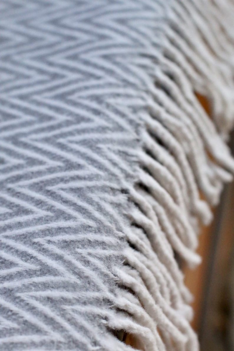 May include: A white blanket with a chevron pattern and fringe trim. The blanket is soft and fluffy, and it would be perfect for cuddling up on the couch.