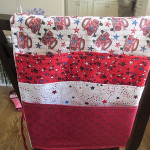 May include: A red, white, and blue fabric chair back organizer with multiple pockets. The fabric features a pattern of stars and red pickup trucks.
