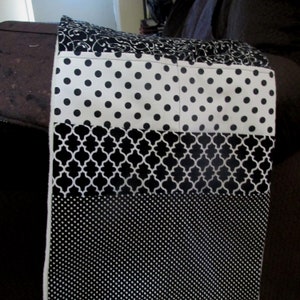 May include: Black and white fabric with a variety of patterns, including polka dots, geometric designs, and a floral pattern. The fabric is sewn together in a patchwork style.